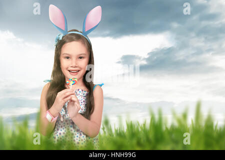 Asian little girl wearing Bunny Ears holding lollipop sur fond d'herbe verte Banque D'Images