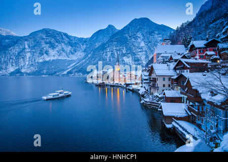 Vue de carte postale classique de la célèbre ville au bord du lac de Hallstatt dans les Alpes avec des passagers à bord d'un navire traditionnel de mystic winter twilight, Salzkammergut, Autriche Banque D'Images