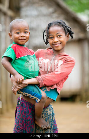 Smiling portrait d'une petite fille malgache tenant son frère dans ses bras pris dans les régions rurales de Fisherman's Village (communauté) le long de la côte en Fort-Daup Banque D'Images