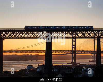 Passage à niveau du Train de voyageurs le pont du Forth avec la Route des ponts derrière au coucher du soleil au nord Queensferry Fife Ecosse Banque D'Images