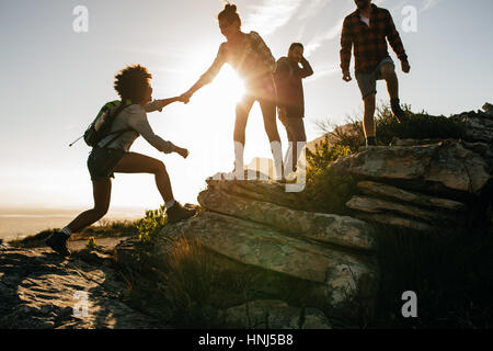 Groupe de randonneurs sur une montagne. Femme d'aider son amie à escalader un rocher. Les jeunes en montagne randonnée au coucher du soleil. Banque D'Images