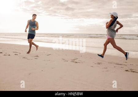 Jeune homme et femme s'exécutant en matinée sur la plage. Couple tout en courant sur la côte. Banque D'Images