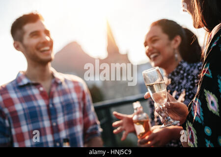 Les amis se tenant ensemble sur le toit avec un verre et bavarder. Les jeunes hommes et femmes ayant une partie sur le toit. Se concentrer sur le verre à champagne dans la main des femmes. Banque D'Images