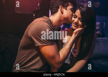 Jeune couple dans l'amour à la boîte de nuit. L'homme s'embrasser sa petite amie assise à un bar-salon. Banque D'Images