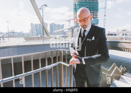 Moyen-âge homme contemporain piscine dans la ville à l'aide de smart phone smart et watvch - technologie, affaires, concept multitâche Banque D'Images