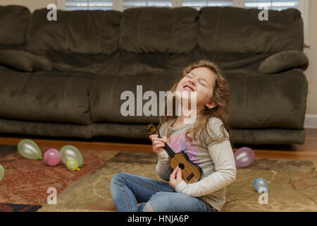 Petite fille jouant un ukulele dans son salon-de-chaussée Banque D'Images