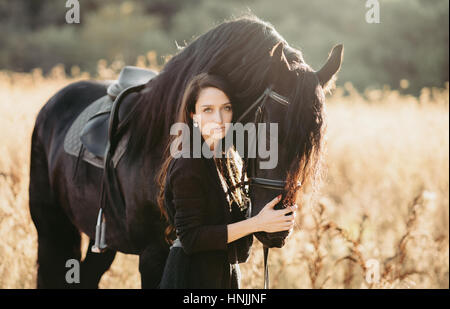 Portrait jeune femme portant des vêtements noirs, caressant son cheval noir Banque D'Images