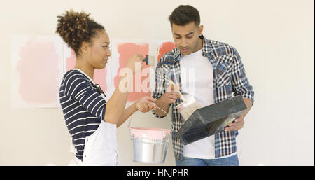 Jeune couple essaie différentes teintes de peinture pour décorer leur nouvel appartement de le mélanger dans un seau et l'application au mur nuances Banque D'Images