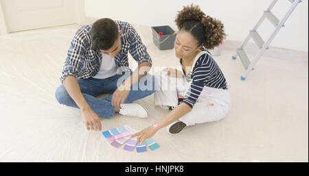 Jeune couple looking at paint swatches pour décorer leur nouvelle maison assis sur le plancher dans la salle de séjour Banque D'Images