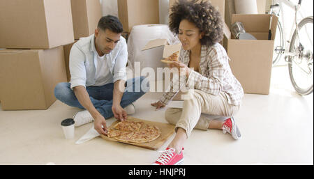 Young African American couple de savourer une pizza, assis sur le sol en face d'un tas de boîtes d'emballage Banque D'Images
