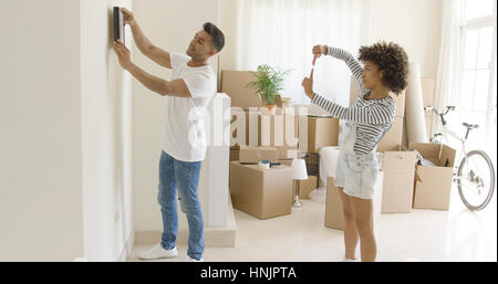 Jeune couple hanging photos dans leur nouvelle maison en l'alignant sur le mur ensemble travailler en équipe Banque D'Images