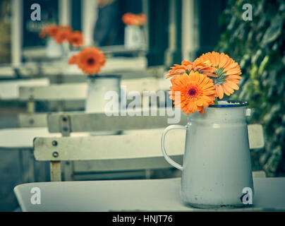 Gerbera Orange daisy fleurs dans un pot en métal sur une table de café à l'extérieur Banque D'Images
