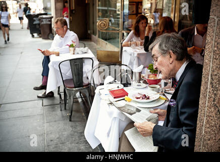 Elder Newyorkese chers tout en lisant le journal après le déjeuner dans le centre-ville de Manhattan. Banque D'Images