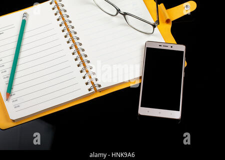 Vue de dessus d'un carnet de notes, lunettes, stylo et smartphone sur un fond noir. Close-up Banque D'Images