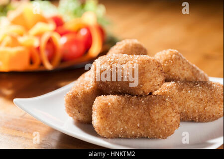 Croquettes d'aubergines sur un plateau carré blanc sur un fond de bois et d'une salade Banque D'Images