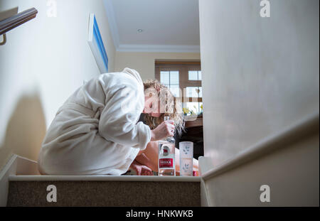 Femme assise enfoncée dans sa robe de chambre à la maison pendant la journée à boire fortement traiter eux-Photographie - posée par model Banque D'Images