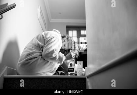 Femme assise enfoncée dans sa robe de chambre à la maison pendant la journée à boire fortement traiter eux-Photographie - posée par model Banque D'Images