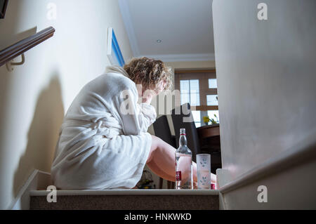 Femme assise enfoncée dans sa robe de chambre à la maison pendant la journée à boire fortement traiter eux-Photographie - posée par model Banque D'Images