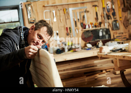 Homme debout dans un atelier d'inspecter de près le bord d'une planche en bois. Banque D'Images