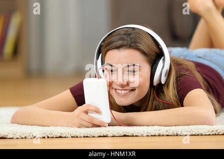 Happy teen regarder du contenu multimédia en ligne dans un smartphone allongé sur un tapis sur le plancher de la salle de séjour à la maison Banque D'Images