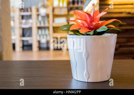 Fleur orange artificielle en pot blanc en céramique sur table en chêne foncé coffee shop, selective focus et l'arrière-plan flou. Banque D'Images