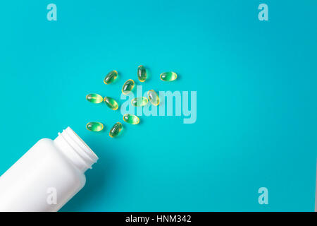 Omega 3 capsules d'huile de poisson s'échappant de la bouteille en plastique blanc sur fond bleu. Banque D'Images