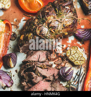 Roastbeef cuit rôti de viande avec légumes et fines herbes en metal plaque de cuisson, vue du dessus, selective focus. Concept de Slow food Banque D'Images