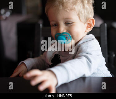 Bébé garçon assis dans une chaise haute et souriant avec sucette restaurant chinois. Banque D'Images