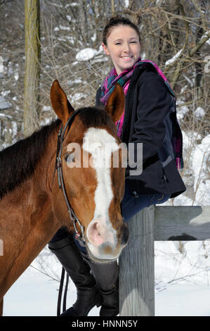 Adolescentes et à cheval, assis et portrait smiling at en hiver la neige et le soleil. Banque D'Images