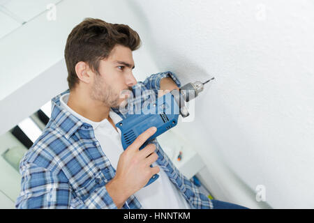 Homme builder perçage de trous dans le mur at construction site Banque D'Images