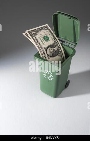Image des billets de banque dans une poubelle de recyclage de jouets poubelle de roues. Métaphore pour le recyclage de l'argent, de l'argent au drain, de l'économie de Biden. Banque D'Images