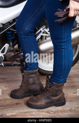 Les jambes des femmes porter un jean bleu et des chaussures de sécurité en cuir brun pour la moto sont près de moto, vue en gros Banque D'Images