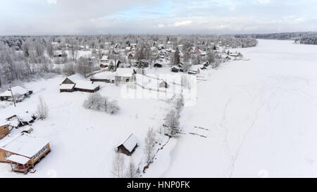 Les empreintes sont sur la glace enneigée du lac gelé près de la rive de l'hiver. Village russe est en bois d'evergreen. Vue aérienne. La Russie Banque D'Images