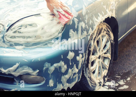 Laver la voiture à la main avec une éponge savonneuse. Le nettoyage de la voiture. Soins pour la voiture concept. Main de l'homme laver la voiture à l'aide de l'éponge avec de la mousse Banque D'Images