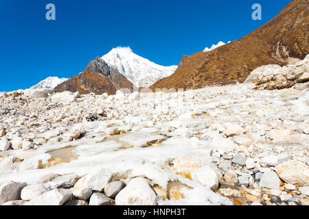 Alpin glacial rivière qui traverse un paysage rocheux blanc à haute altitude la toundra alpine avec Langtang Lirung Kyanjin Gompa pointe près de l'arrière-plan Banque D'Images