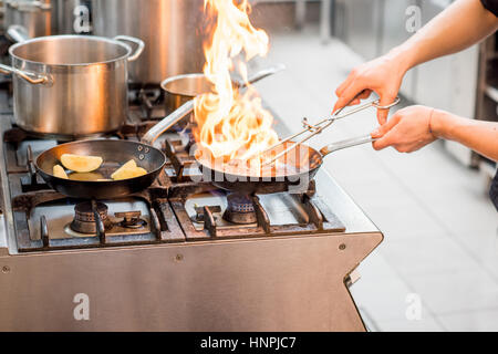 La friture steak viande Chef sur la cuisinière à gaz avec le feu à la cuisine. Vue rapprochée sur la poêle Banque D'Images