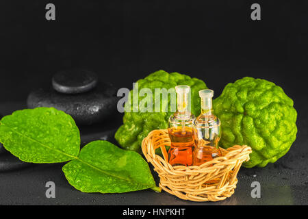 Spa concept de bergamote, Feuille, huile parfum zen et pierres de basalte avec gouttes d'eau sur fond noir, Close up Banque D'Images