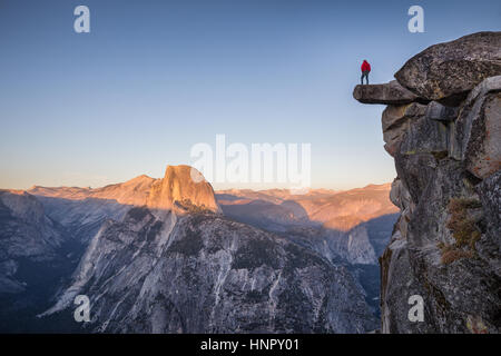 Un male hiker debout sur un rocher en surplomb à Glacier Point profiter de la vue à couper le souffle vers célèbre Demi Dôme dans le magnifique crépuscule au coucher du soleil Banque D'Images