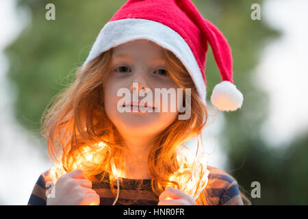 Une petite fille vêtue d'un chapeau de Père Noël et de la féerie de lumières de Noël Banque D'Images