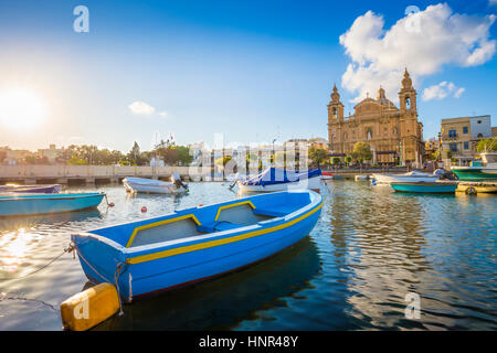 Msida, Malte - Bleu bateau de pêche traditionnel avec la célèbre église paroissiale de Msida sur fond d'une journée d'été avec ciel bleu et nuages Banque D'Images