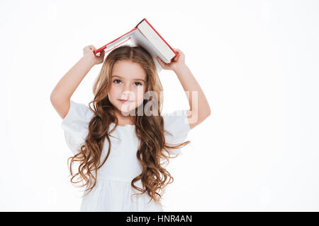 Jolie petite fille curly livre debout et tenant au-dessus de sa tête sur fond blanc Banque D'Images