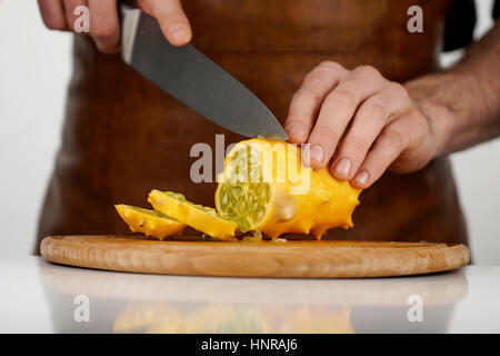 Fruits tropicaux kiwano coupe l'homme en tranches sur une planche à découper en bois sur fond blanc Banque D'Images