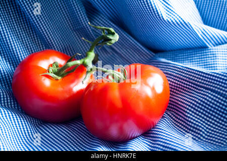 Deux tomates rouges mûres sur un tissu à carreaux bleu et blanc Banque D'Images