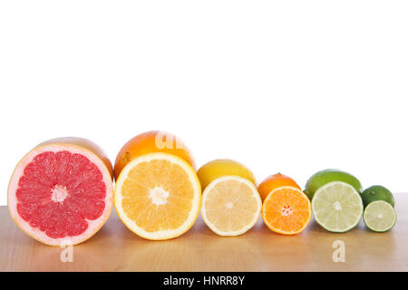 Les agrumes en tranches colorées alignées en rangées sur une table en bois brun clair avec un fond blanc. Pamplemousse, citron, orange marine, citron vert, clémentine cuties Banque D'Images