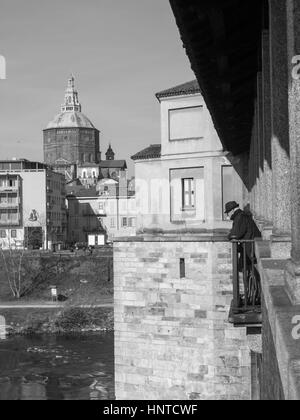 Pavia, Italie - 8 mars 2015 : Pont couvert sur la rivière Tessin. Vieil homme avec chapeau foncé regarder la rivière qui coule sous le pont. Banque D'Images