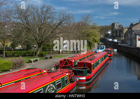 Vue panoramique ensoleillée sur les gens qui marchent sur le chemin d'attelage après les bateaux de location de canal rouge lumineux amarrés - Canal Leeds-Liverpool, Skipton, Yorkshire, Angleterre, Royaume-Uni. Banque D'Images