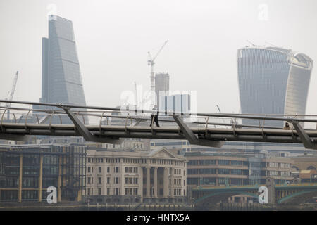 L'homme marchant sur Millennium Bridge avec le talkie walkie et Cheesegrater, gratte-ciel emblématique de la ville de Londres sur un sombre matin d'hiver Banque D'Images