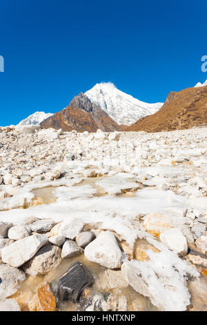 Alpin glacial rivière qui traverse un paysage rocheux blanc à haute altitude la toundra alpine avec Langtang Lirung Kyanjin Gompa pointe près de l'arrière-plan Banque D'Images