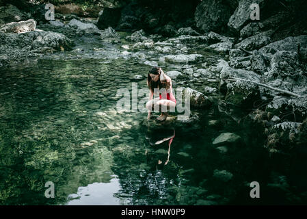 Caucasian woman crouching sur rochers à l'eau de piscine Banque D'Images