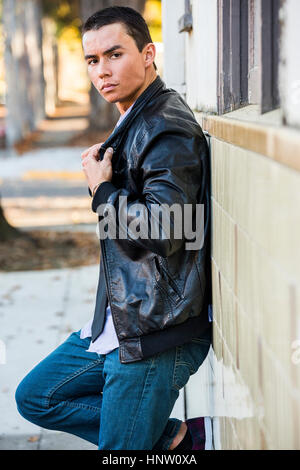 Serious Mixed Race man leaning on wall portant veste en cuir Banque D'Images